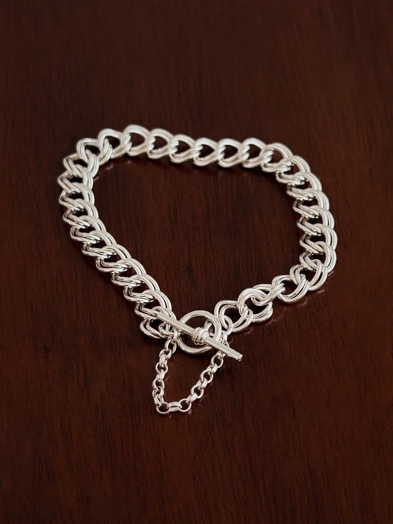 Silver bracelet chain with a t bar closure and safety chain on a wooden surface
