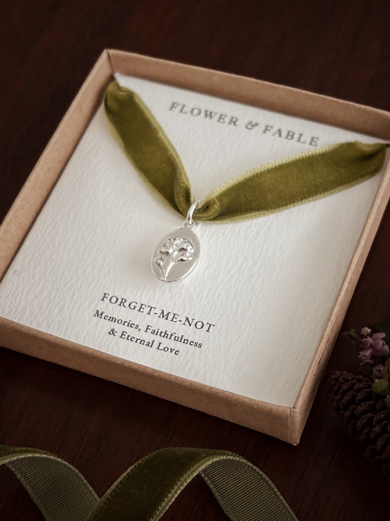 Necklace with a silver forget-me-not pendant on green velvet ribbon in a 'Flower & Fable' box.