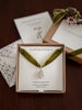 Green velvet necklace with silver pendant in a 'Flower & Fable' box and a love note on a wooden surface.