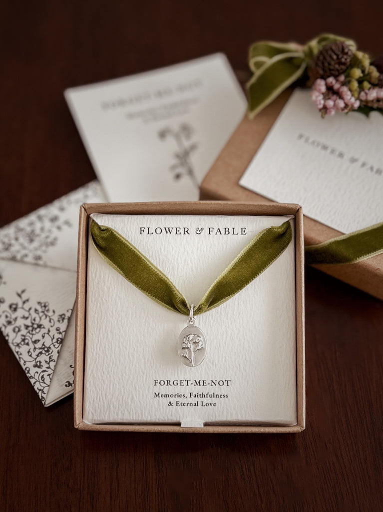 Green velvet necklace with silver pendant in a 'Flower & Fable' box and a love note on a wooden surface.