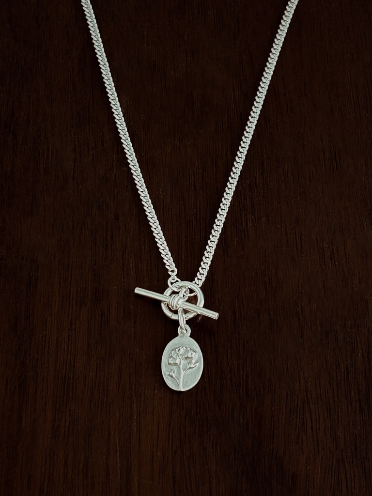 Sterling Silver Curb necklace with t-bar closure with a flower pendant on a dark wooden background