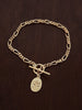 Gold forget me not charm bracelet with figaro chain and t bar closure on a dark wooden surface