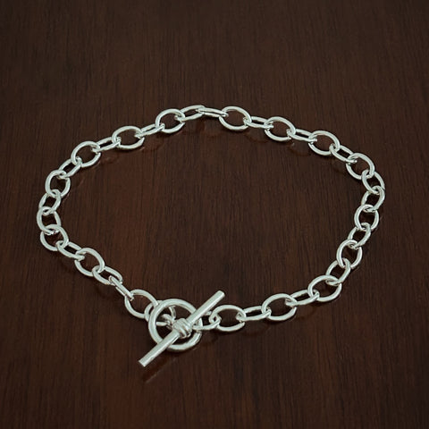Heavy trace Silver chain bracelet with a t bar closure on a wooden surface