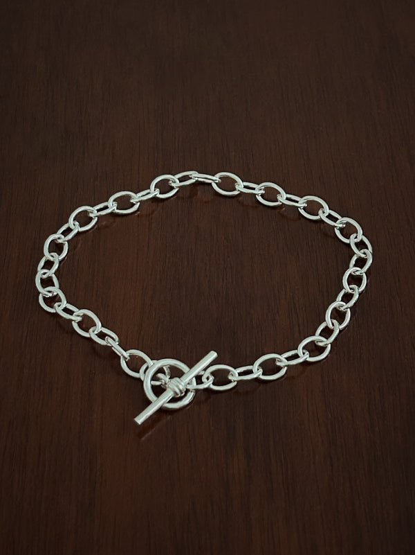 Heavy trace Silver chain bracelet with a t bar closure on a wooden surface