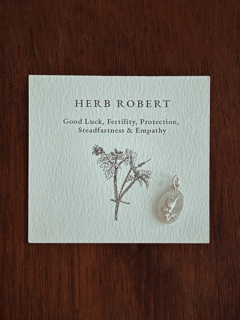 Card with 'Herb Robert' description and a pendant on a wooden surface