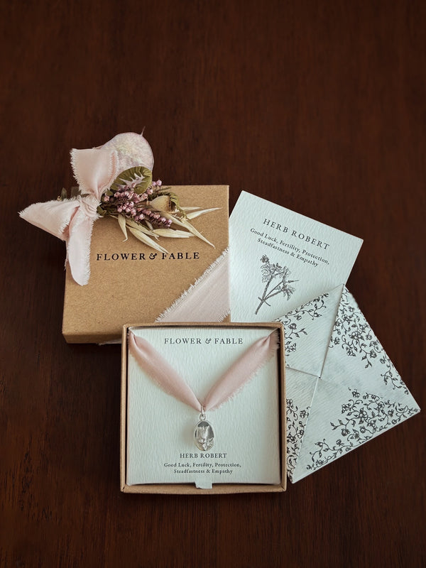 Flower & Fable silver flower necklace packaging with pink ribbon and decorative elements on a wooden surface