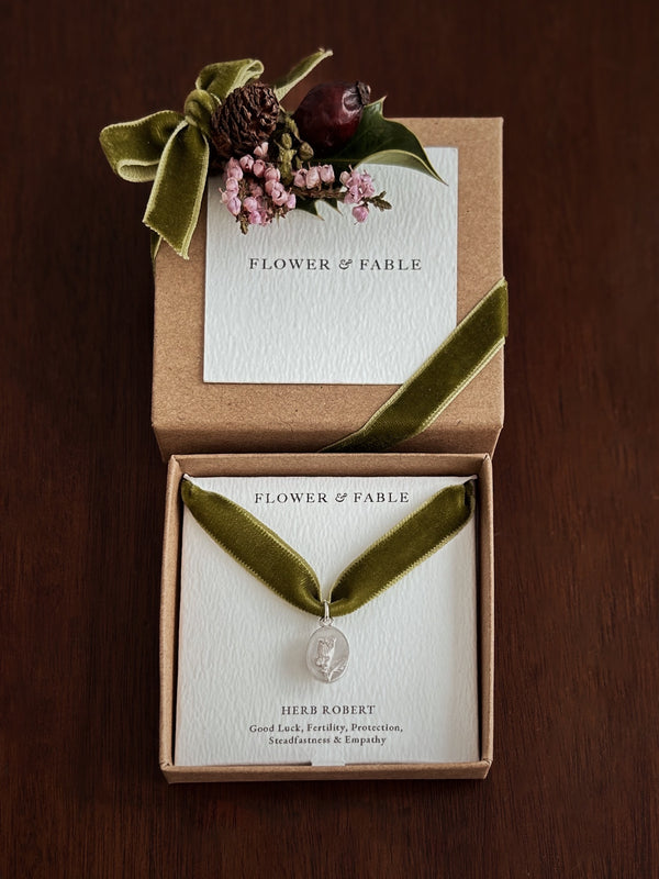 Green velvet ribbon necklace with a silver flower charm in a 'Flower & Fable' box on a wooden surface