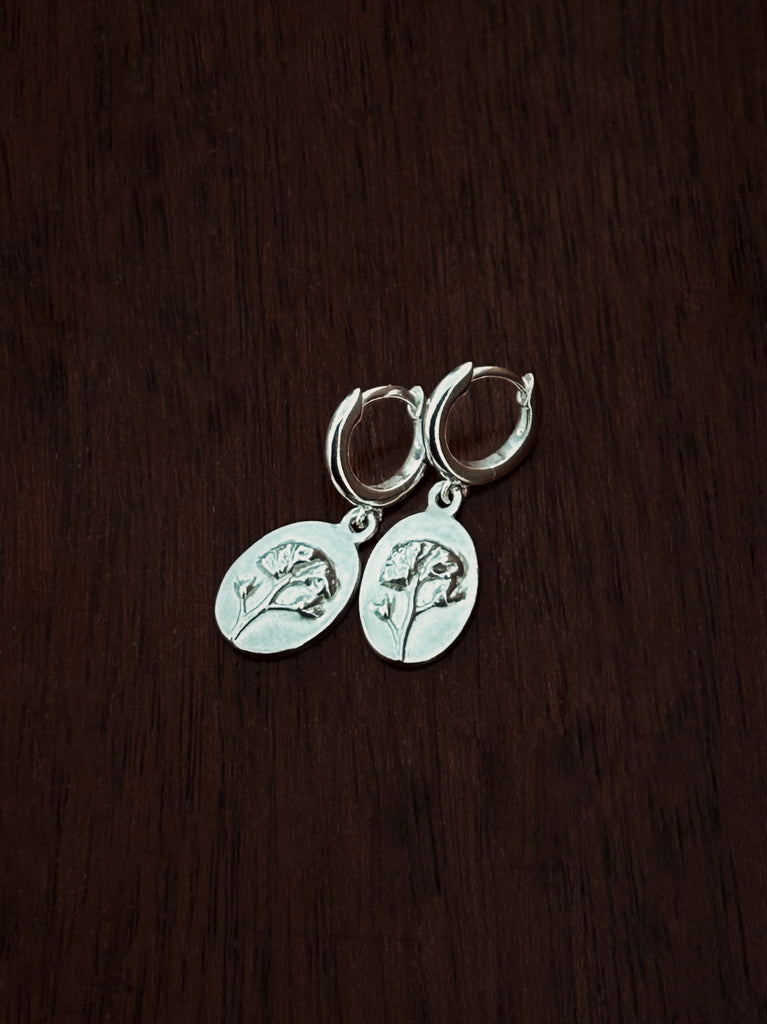 Silver huggie hoop earrings with flower charms on a dark wooden surface