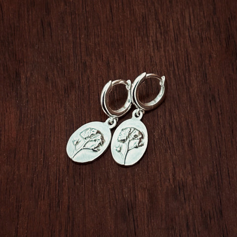 Silver huggie hoop earrings with flower charms on a dark wooden surface