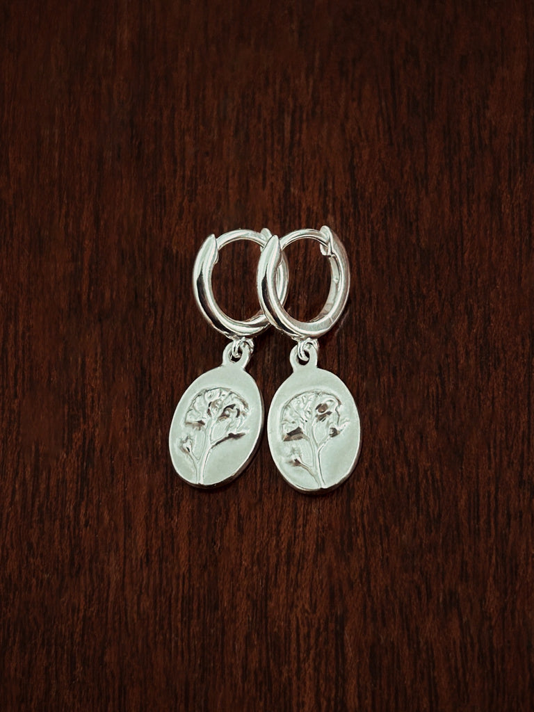 Silver hoop dangle charm earrings on a dark wooden surface
