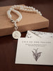 Pearl necklace with a lily coin charm on a card with text and illustration, on a brown surface