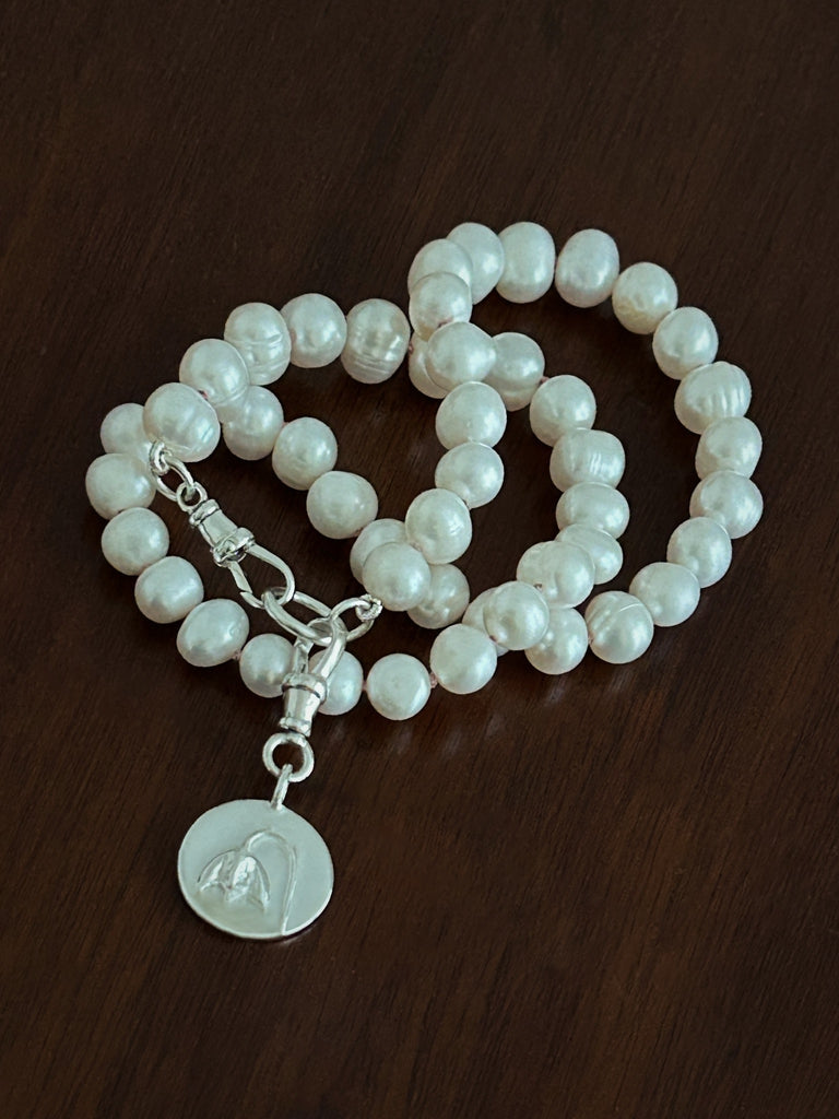 Pearl bracelet with a silver charm on a wooden surface