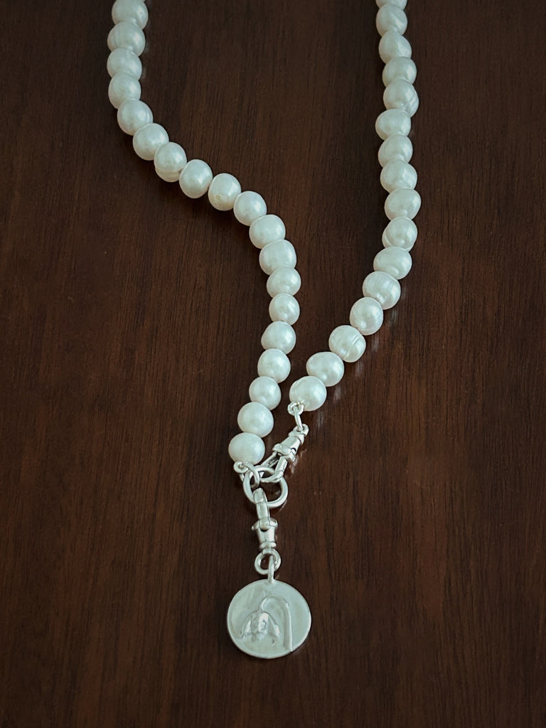 Pearl necklace with a silver pendant on a wooden surface