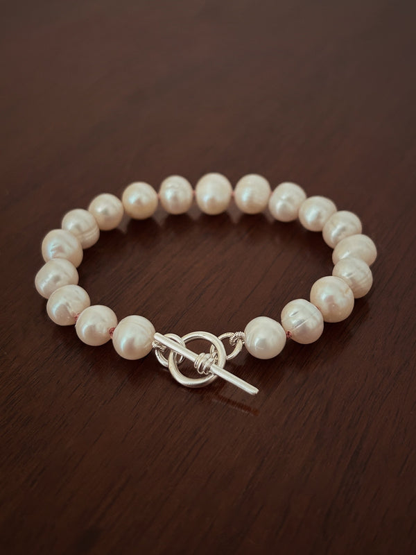 Pearl bracelet with a silver t-bar closure on a wooden surface