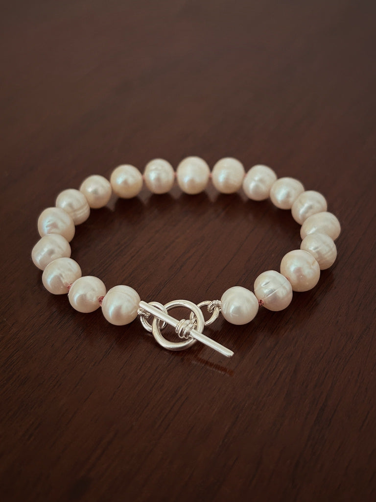 Pearl bracelet with a silver t-bar closure on a wooden surface