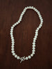 Hand-knotted freshwater pearl necklace on dark pink silk, shown with sterling silver T-bar clasp on linen background.