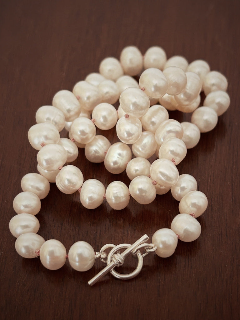 Classic pearl necklace worn at choker length, showing natural sheen and delicate silk knotting.