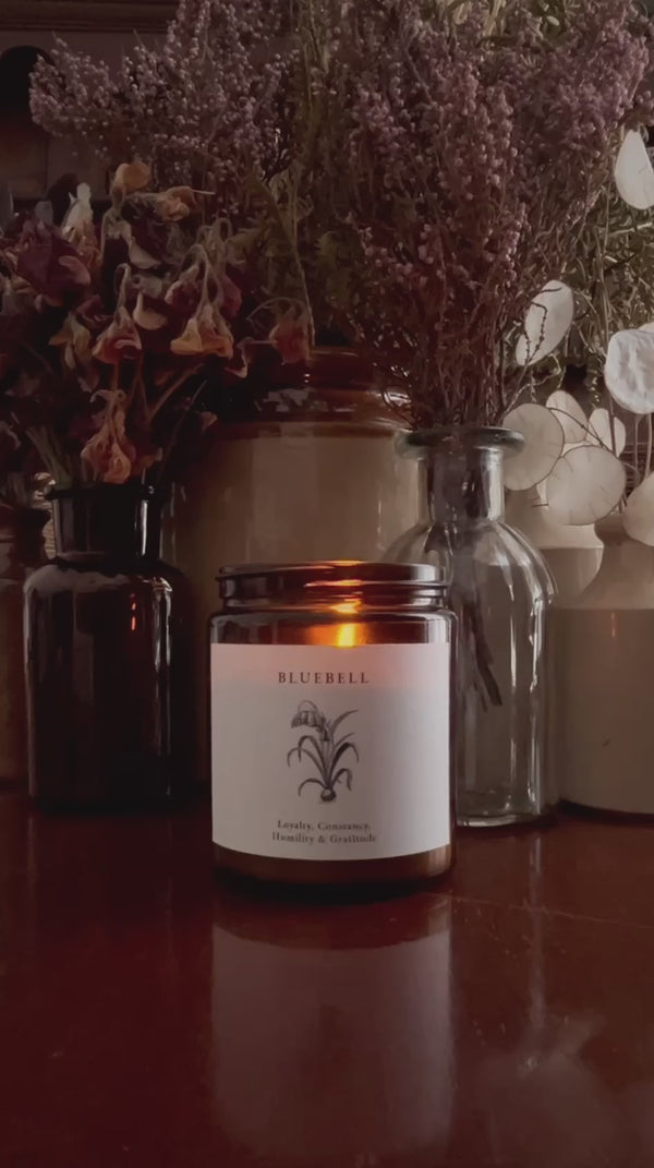 Video of a hand poured soy candle in amber glass with a crackling wood wick